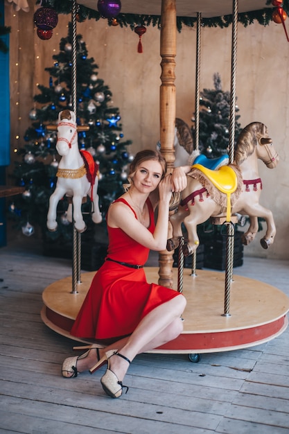 Hermosa joven se regocija cerca de un carrusel con caballos. Navidad.