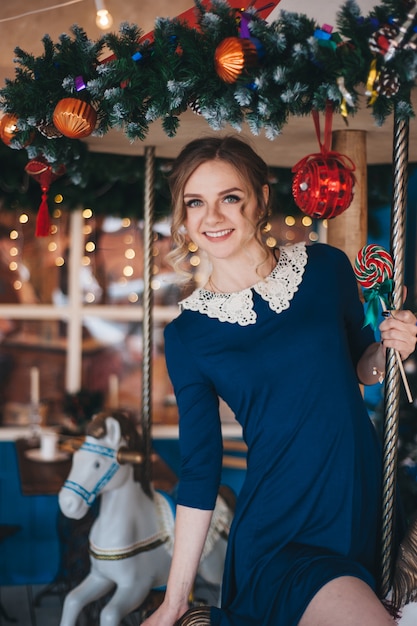 Hermosa joven se regocija cerca de un carrusel con caballos. Navidad.