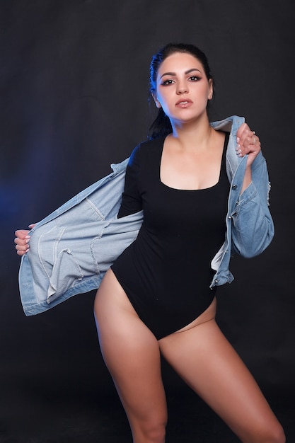 Hermosa joven regordeta en cuerpo negro de pie sobre un fondo negro. Plus size modelo de moda sexy en lencería, mujer gorda sobre fondo negro de estudio, cuerpo de la mujer con sobrepeso, retrato de cuerpo entero