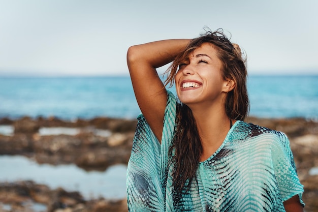 Una hermosa joven se relaja en la playa en un día soleado. Ella está posando manteniendo los ojos cerrados con una sonrisa en su rostro.