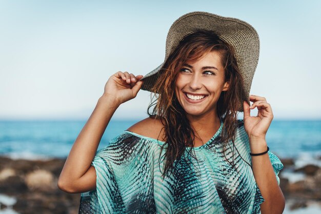 Una hermosa joven se relaja en la playa en un día soleado. Ella está posando y mirando lejos con una sonrisa en su rostro.