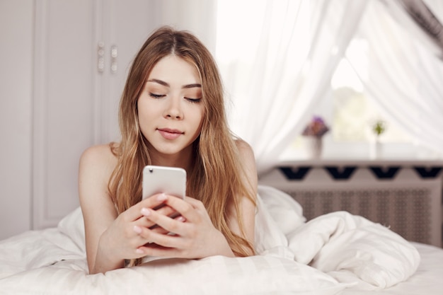 Hermosa joven relajante en la cama con su teléfono inteligente