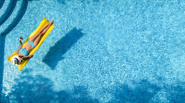 Hermosa joven relajante en la piscina, la mujer nada en un colchón inflable y se divierte en el agua en vacaciones familiares, complejo vacacional tropical, vista aérea desde arriba