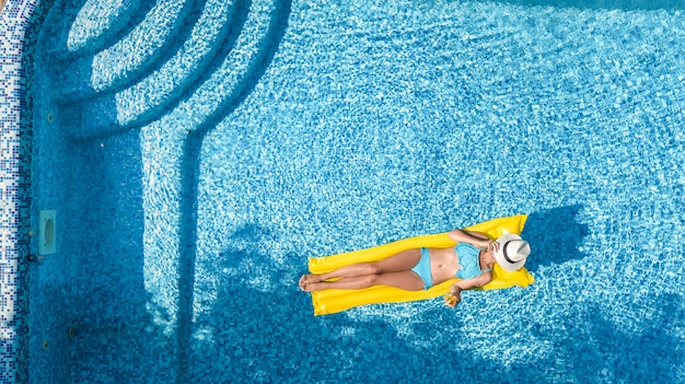 Hermosa joven relajante en la piscina, nada en un colchón inflable y se divierte en el agua en vacaciones familiares, resort de vacaciones tropical, vista aérea de aviones no tripulados desde arriba