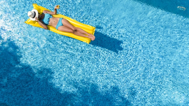 Hermosa joven relajante en la piscina, nada en un colchón inflable y se divierte en el agua en vacaciones familiares, resort de vacaciones tropical, vista aérea de aviones no tripulados desde arriba