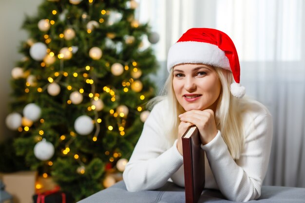 Hermosa joven rezando delante del árbol de Navidad decorado