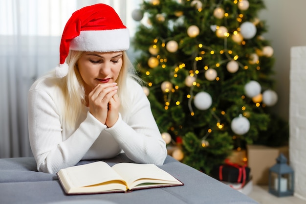 Hermosa joven rezando delante del árbol de Navidad decorado