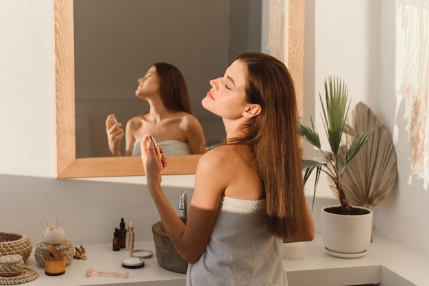 Foto una hermosa joven rocía perfume en su cuello mientras está de pie en el baño