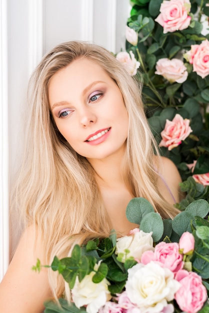 Hermosa joven romántica con maquillaje natural. Rosas rosadas y blancas pálidas con vegetación. Concepto de perfumería y cosmética.