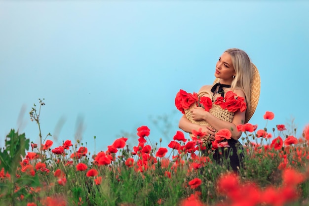 Hermosa joven rubia camina en un campo florido de amapolas al atardecer