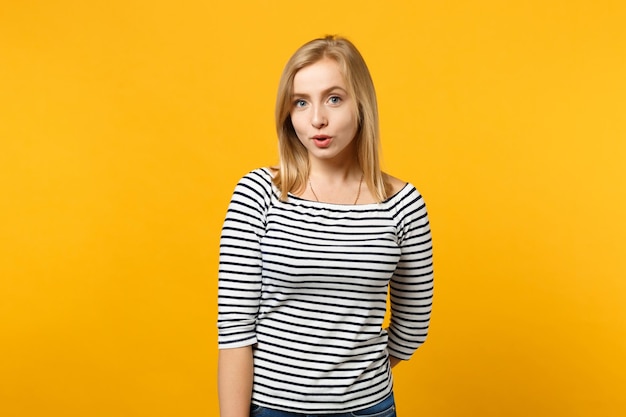 Hermosa joven rubia confundida con ropa a rayas mirando una cámara aislada en un fondo de pared naranja amarillo brillante, retrato de estudio. Gente emociones sinceras concepto de estilo de vida. Simulacros de espacio de copia