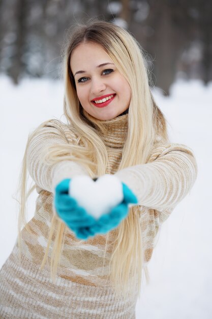 Hermosa joven rubia con un corazón hecho de nieve en sus manos