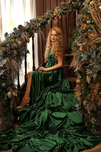 Hermosa joven rubia con un elegante vestido verde en las escaleras decoradas para Navidad año nuevo