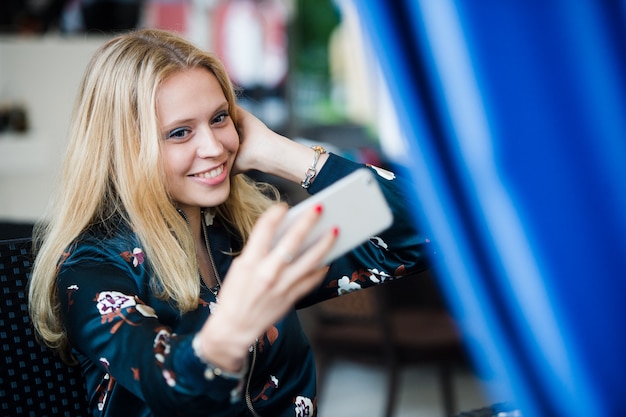 Hermosa joven rubia mujer caucásica tomando un selfie con smartphone al aire libre en la cafetería de verano