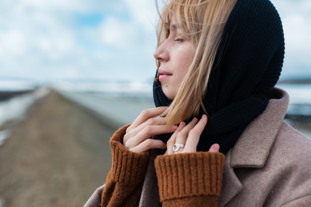 Hermosa joven rubia con un pañuelo negro se encuentra en medio de la carretera con los ojos cerrados contra el cielo azul.