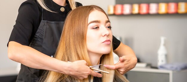 Hermosa joven rubia con el pelo rubio largo y recto cortándose el pelo en la peluquería