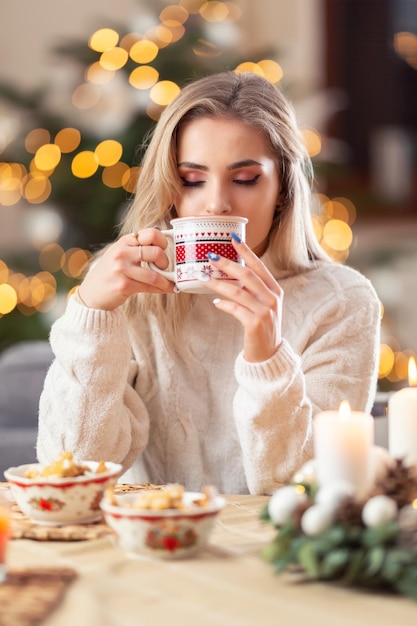 Una hermosa joven rubia prueba el té de ponche navideño o el café o el vino caliente