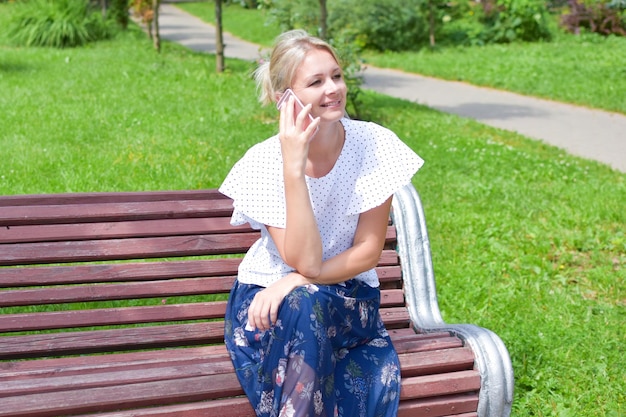 Hermosa joven rubia sentada en un banco al aire libre con teléfono