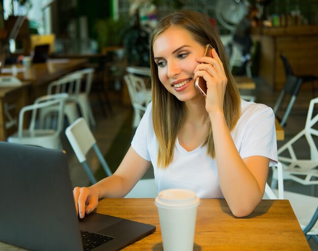 Hermosa joven rubia sentada en una cafetería y trabajando en la computadora