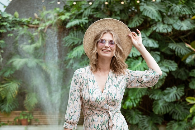 Hermosa joven rubia con un sombrero de paja y gafas posando en el parque