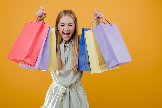 Hermosa joven rubia sonriendo con coloridas bolsas aisladas sobre amarillo