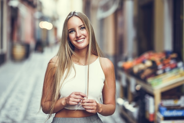 Foto hermosa joven rubia sonriendo en el fondo urbano.