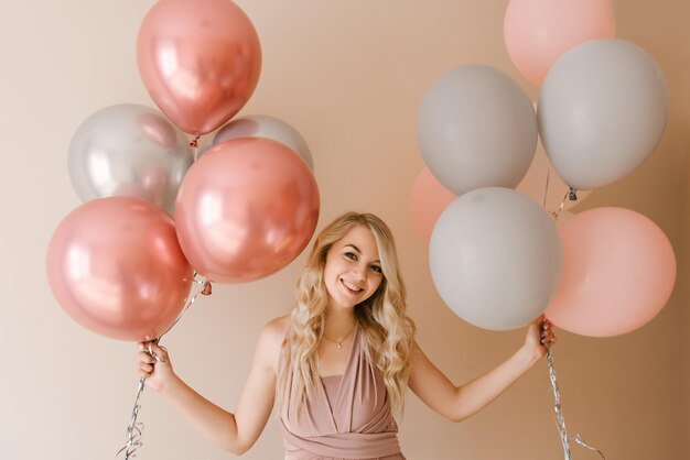 Hermosa joven rubia sonriente con globos blancos grises y rosas sobre un fondo claro