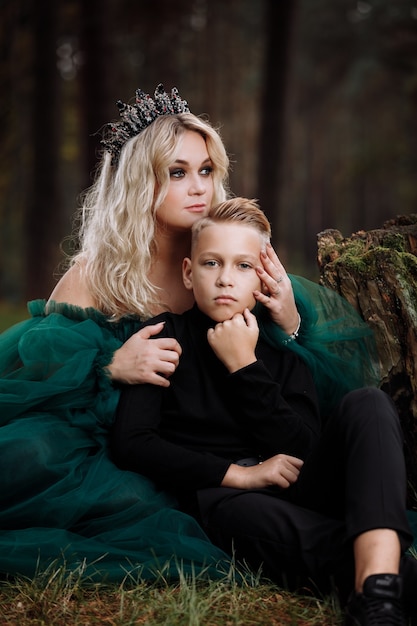 Foto una hermosa joven rubia con un vestido largo verde y una diadema en la cabeza con un elegante hijo en el bosque.