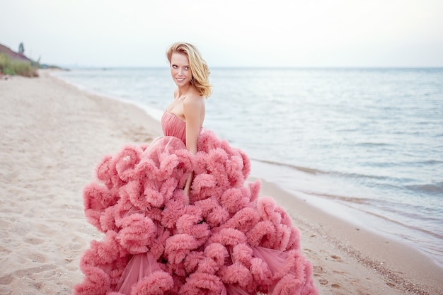 Hermosa joven rubia con vestido rosa en la playa