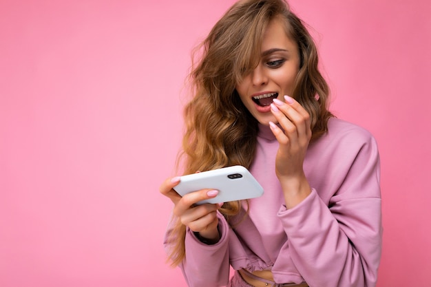 Hermosa joven rubia vistiendo sudadera con capucha rosa aislado sobre fondo rosa con espacio de copia