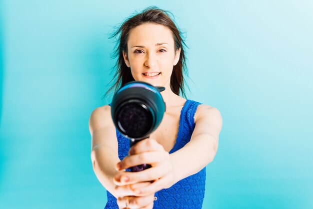 Hermosa joven secándose el cabello con secador de pelo sonriendo con fondo azul.