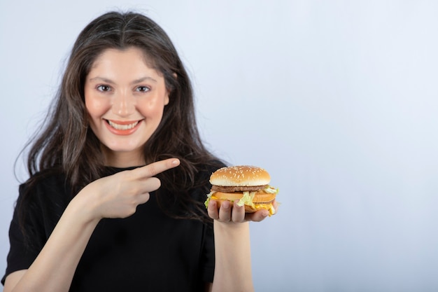 hermosa joven señalando deliciosa hamburguesa de carne.