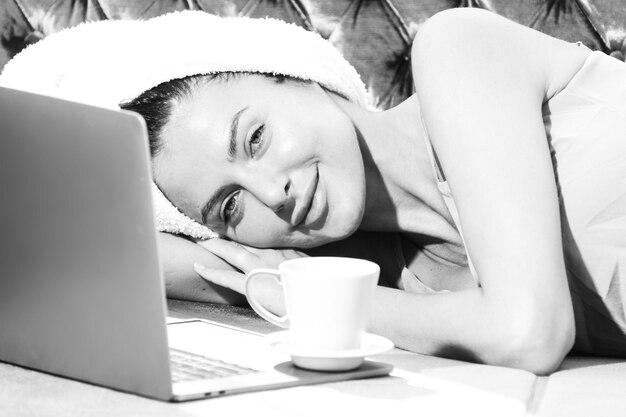 Hermosa joven sensual con café y portátil en pijama disfrutando del tiempo libre matutino en la cama