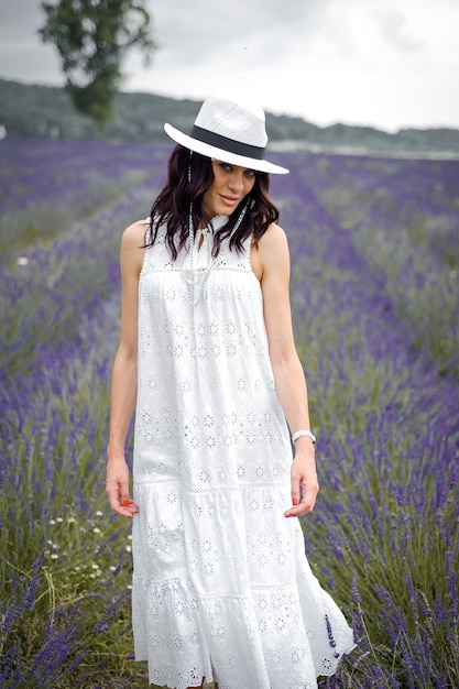 Hermosa joven sensual con sombrero y vestido blanco en el campo de lavanda
