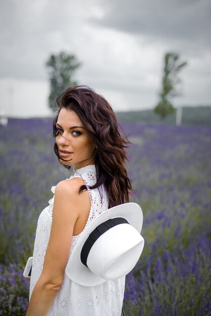 Hermosa joven sensual con sombrero y vestido blanco en el campo de lavanda