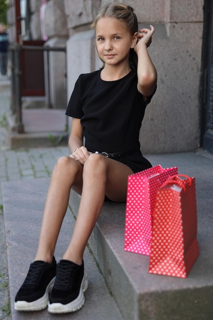 Hermosa joven sentada con bolsas de colores en los escalones de la tienda