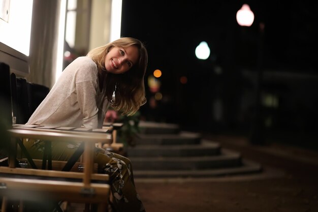 Hermosa joven sentada en un café de la calle por la noche