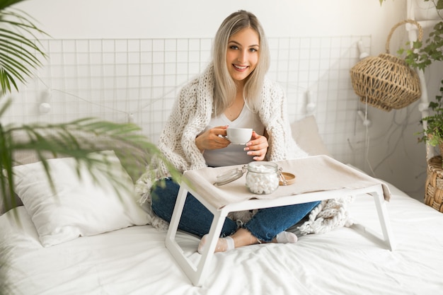 Hermosa joven sentada en la cama con una taza de té