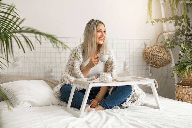 Hermosa joven sentada en la cama con una taza de té