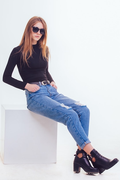 Foto hermosa joven sentada en un cubo blanco en el estudio con aislamiento.