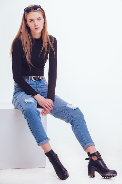 Foto hermosa joven sentada en un cubo blanco en el estudio con aislamiento.