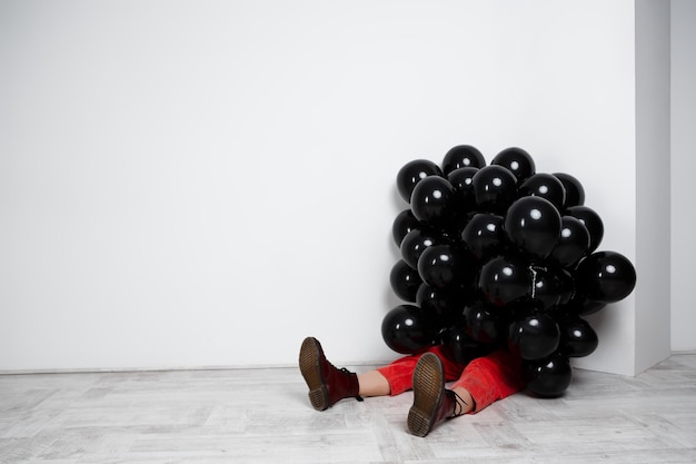 Hermosa joven sentada en globos negros sobre pared blanca