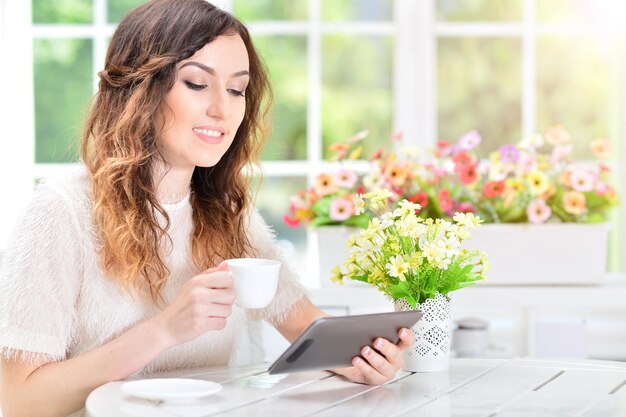 Hermosa joven sentada a la mesa y usando tableta digital