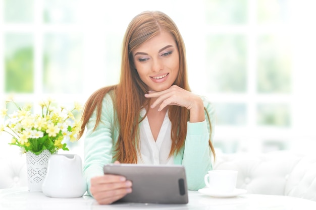 Hermosa joven sentada a la mesa y usando tableta digital