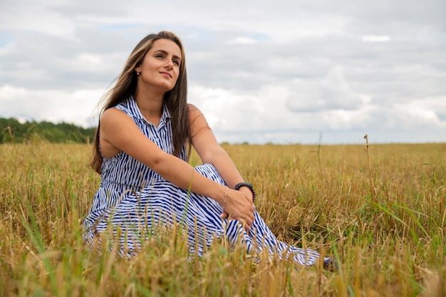 Hermosa joven sentada en un prado de flores en un día soleado de verano y sonríe