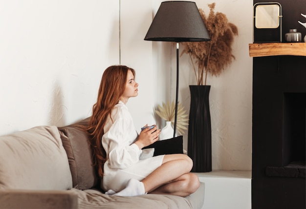 Hermosa joven sentada en el sofá con una taza de café en sus manos