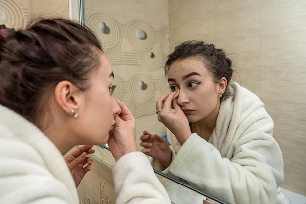 Hermosa joven sexy corrige su maquillaje que fue borrado en una bata de baño Concepto de maquillaje