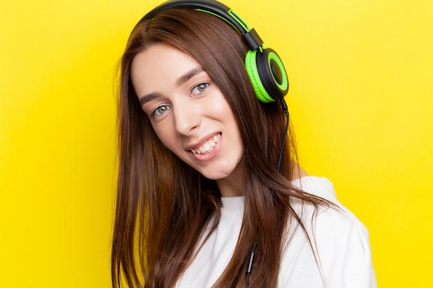 Hermosa joven sexy DJ escuchando música en auriculares verdes sobre un amarillo