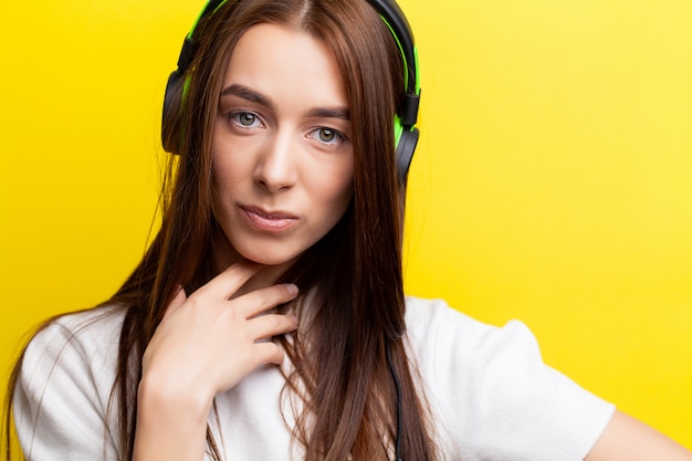 Hermosa joven sexy DJ escuchando música en auriculares verdes sobre un amarillo