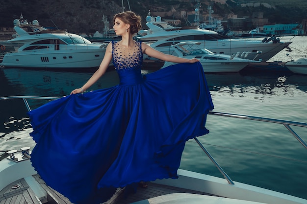 Hermosa joven sexy en un vestido y maquillaje, viaje de verano en un yate con velas blancas en el mar o el océano